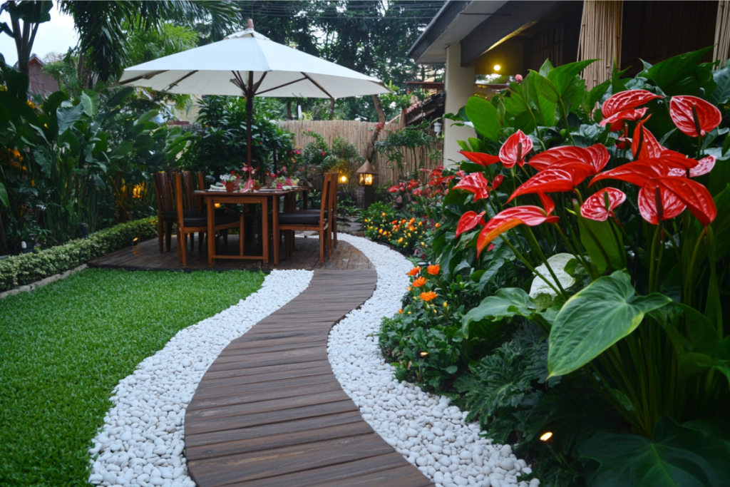 Vibrant red anthurium plants along a garden path with a cozy dining setup, surrounded by lush greenery and outdoor decor.