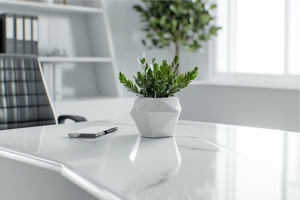 A modern ZZ plant in a geometric white pot on a sleek white office desk, showcasing an elegant and minimalistic office environment.