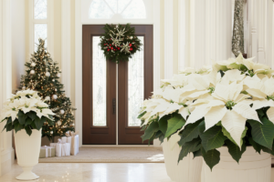 Grand foyer featuring a holiday-decorated Christmas tree alongside symmetrical displays of white poinsettias in tall, white urns for a luxurious entrance.